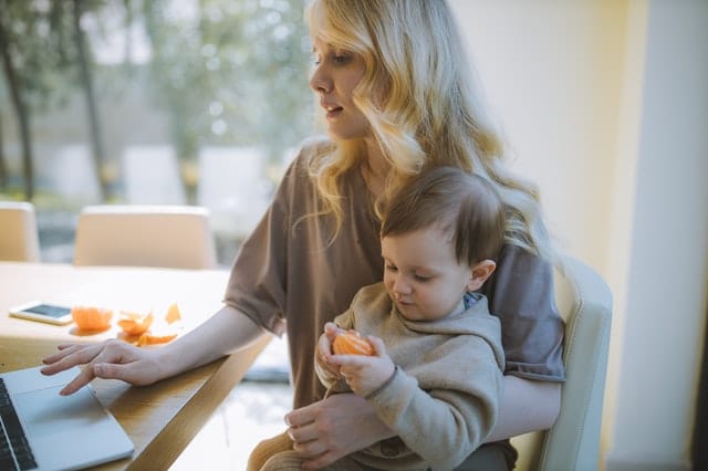 woman carrying her baby and working on a laptop 4079283